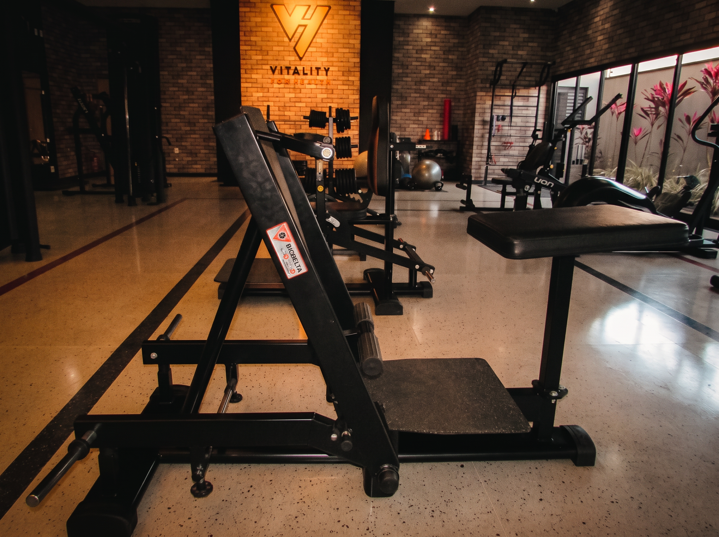 Sala de musculação do Studio Vitality for Health com aparelhos premium e parede iluminada com a logo VH